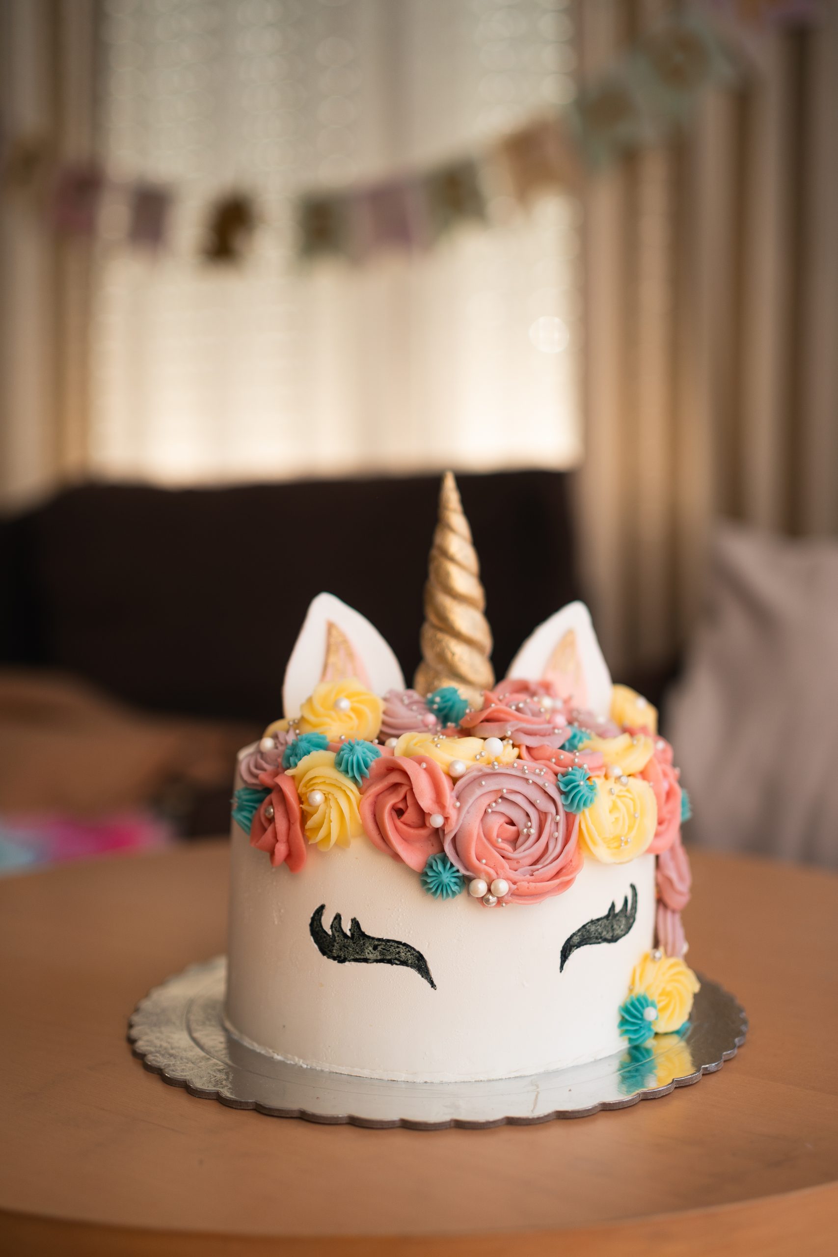 A whimsical unicorn-themed cake adorned with colorful frosting roses and a golden horn takes center stage on a birthday celebration table